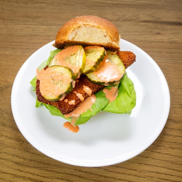P'unk Burger's fried chicken sandwich with pickles, lettuce, and special sauce on a white plate.
