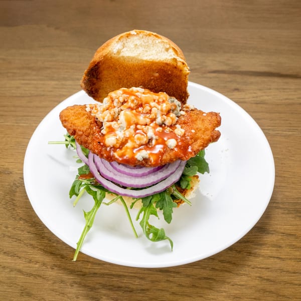 P'unk Burger's buffalo chicken sandwich with blue cheese, red onion, and arugula on a white plate.