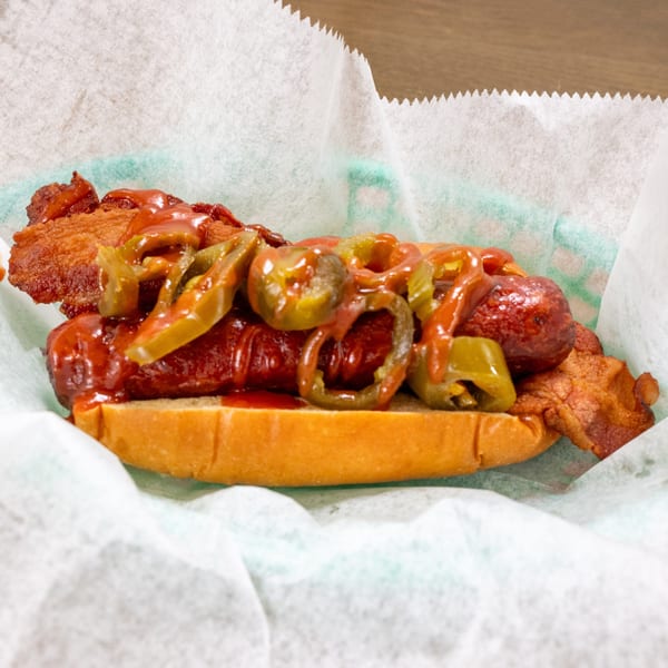 P'unk Burger's hot dog with bacon, ketchup, and sliced jalapeños in a paper-lined basket.