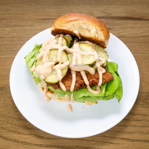 P'unk Burger's fried chicken sandwich with pickles, lettuce, and special sauce on a white plate.