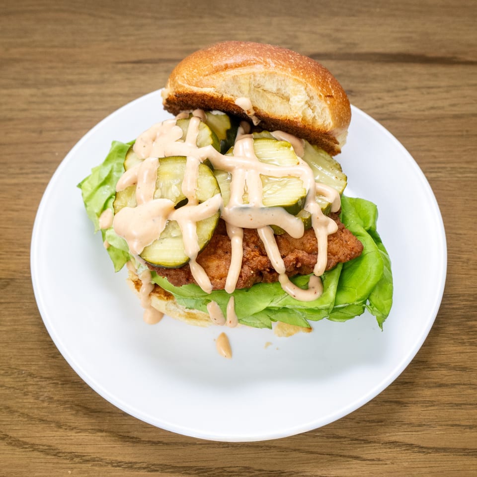P'unk Burger's fried chicken sandwich with pickles, lettuce, and special sauce on a white plate.
