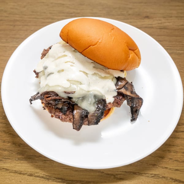 P'unk Burger's mushroom burger, topped with melted white cheese, on a white plate.