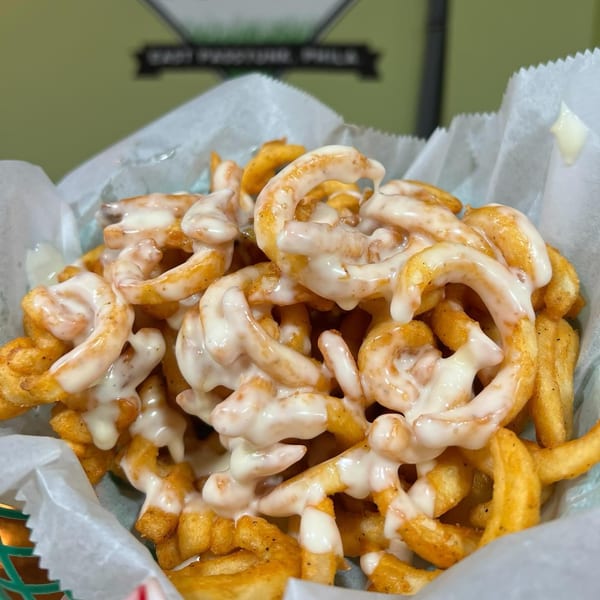 Close-up of P'unk Burger's curly fries, generously topped with creamy white sauce, in a paper-lined basket.